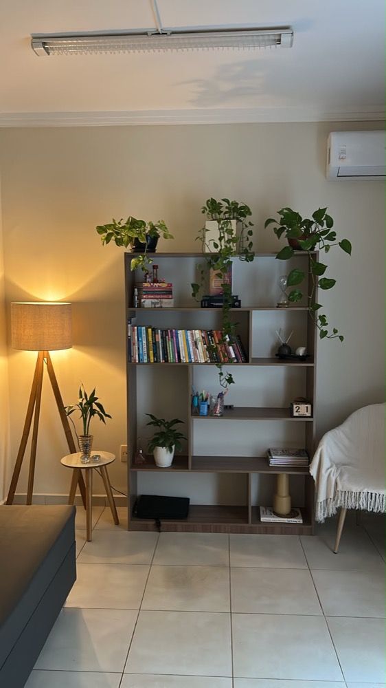Consultório da Stephânia: estante com livros e plantas, luminária e poltrona com manta