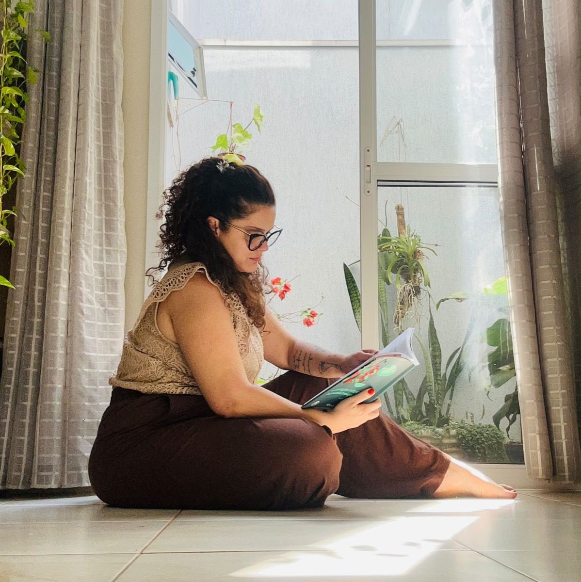 Stephânia sentada ao lado da janela lendo um livro de Terapia Cognitivo-Comportamental